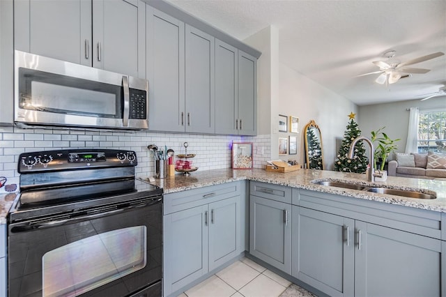 kitchen featuring light stone counters, gray cabinetry, a sink, black electric range oven, and stainless steel microwave