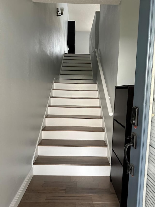 staircase with baseboards, wood finished floors, and a textured ceiling