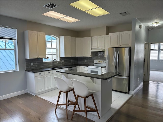 kitchen with dark countertops, freestanding refrigerator, white range with electric stovetop, and visible vents