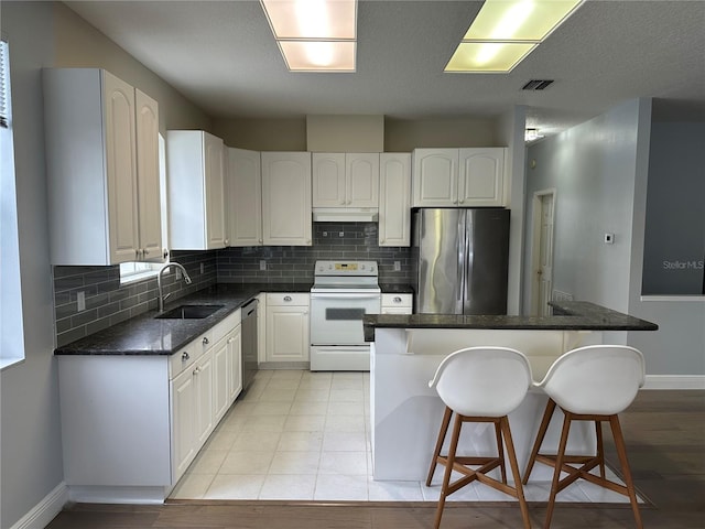 kitchen featuring white cabinets, under cabinet range hood, a kitchen bar, stainless steel appliances, and a sink