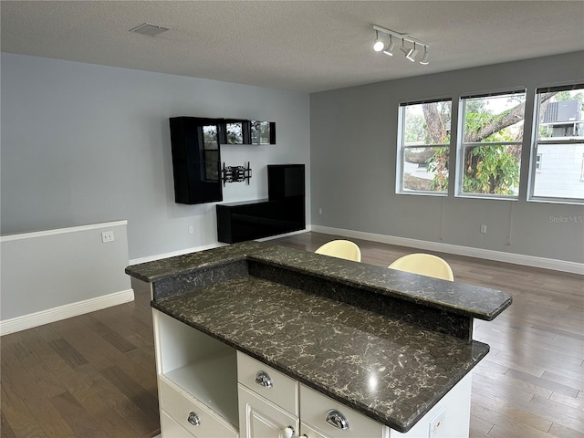 kitchen featuring visible vents, baseboards, a textured ceiling, white cabinetry, and wood finished floors