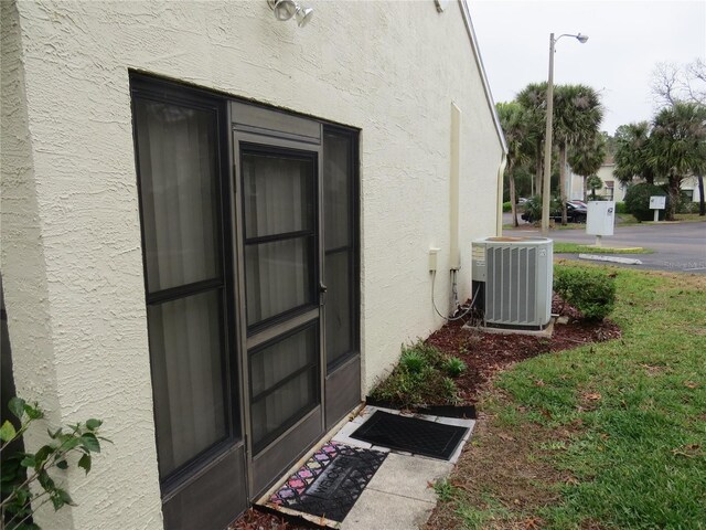 entrance to property with a lawn, cooling unit, and stucco siding