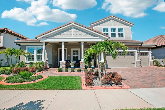 view of front of house featuring stucco siding, decorative driveway, a porch, a garage, and a tiled roof