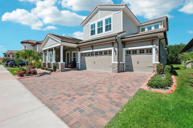 view of front of house with stone siding, a porch, decorative driveway, and a garage