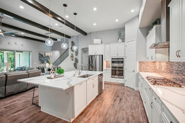 kitchen featuring tasteful backsplash, wall chimney range hood, wood finished floors, stainless steel appliances, and a sink