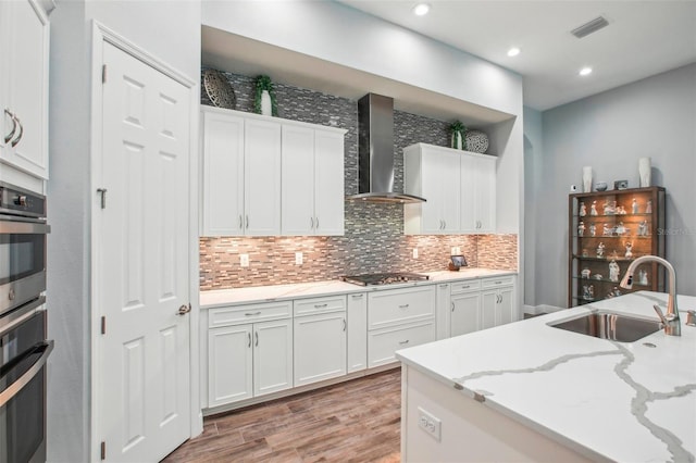 kitchen with visible vents, a sink, appliances with stainless steel finishes, wall chimney exhaust hood, and tasteful backsplash