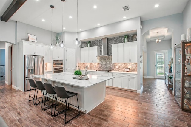 kitchen featuring backsplash, a spacious island, arched walkways, appliances with stainless steel finishes, and wall chimney range hood