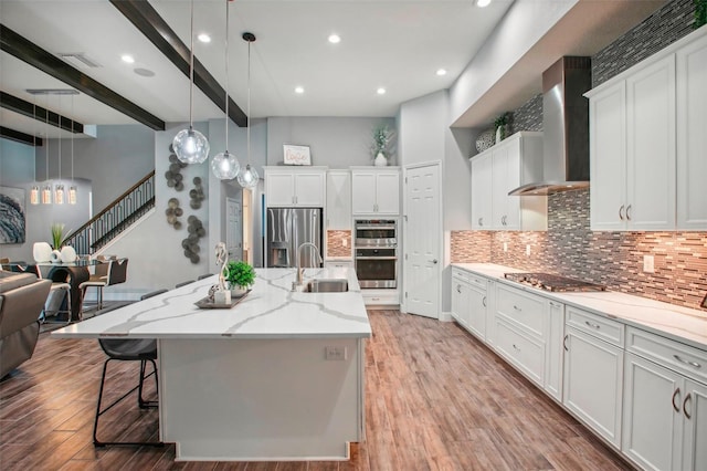 kitchen featuring a sink, wall chimney range hood, light wood finished floors, and stainless steel appliances