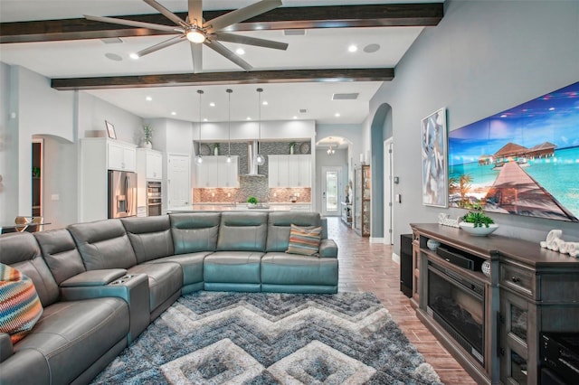 living area featuring beamed ceiling, visible vents, light wood-type flooring, arched walkways, and baseboards