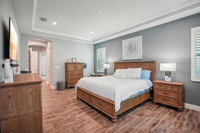 bedroom with a raised ceiling, arched walkways, visible vents, and wood tiled floor