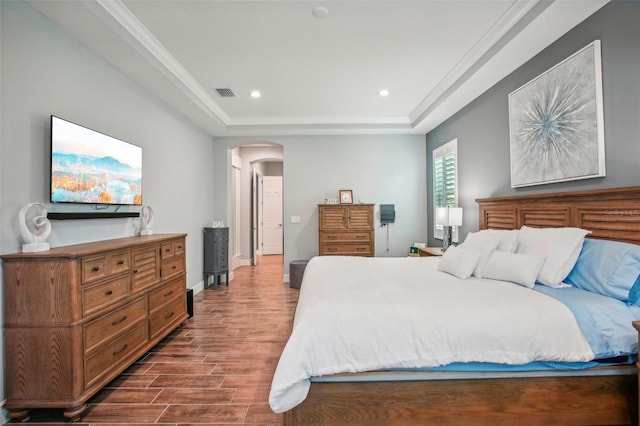 bedroom with visible vents, wood finished floors, baseboards, arched walkways, and a raised ceiling