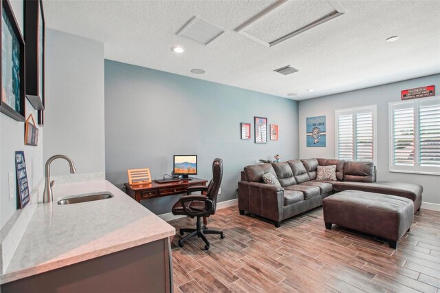 office featuring visible vents, a sink, a textured ceiling, attic access, and wood tiled floor