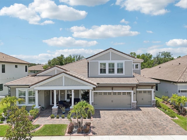 view of front facade with a porch, stone siding, a tiled roof, and decorative driveway