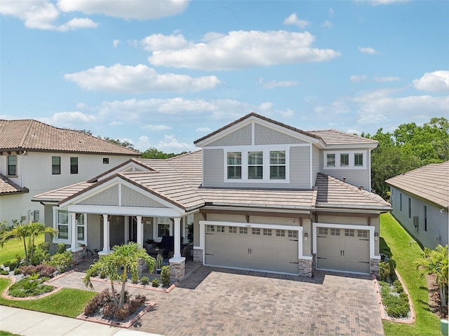 view of front of house with decorative driveway, stone siding, covered porch, and a tile roof