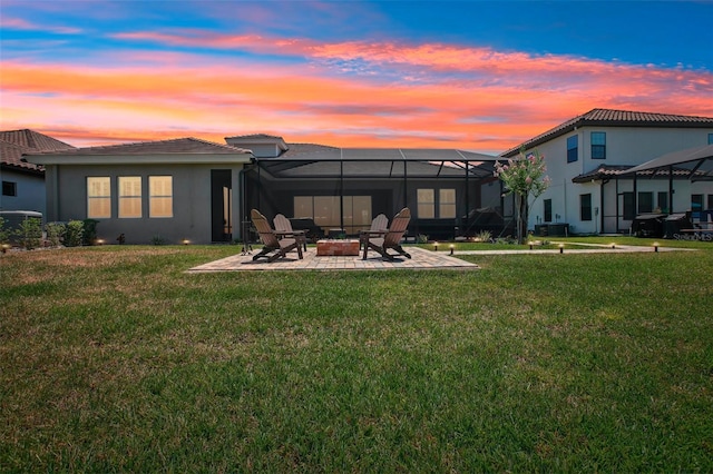 back of house at dusk with a yard, glass enclosure, a fire pit, and a patio