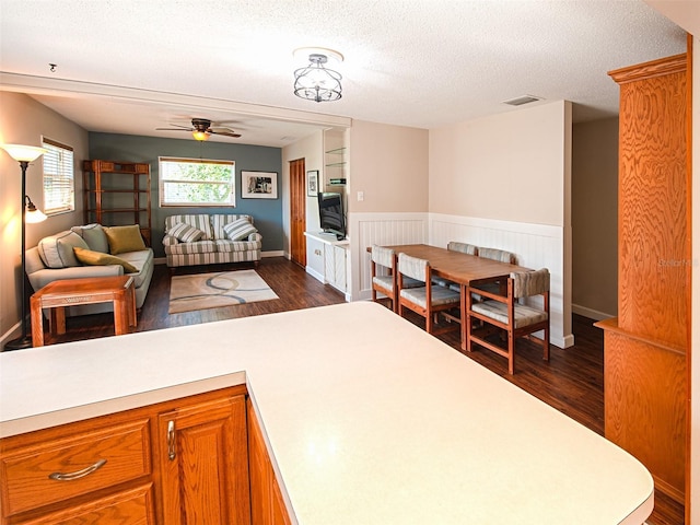 interior space with a textured ceiling, dark wood-style flooring, visible vents, a ceiling fan, and wainscoting