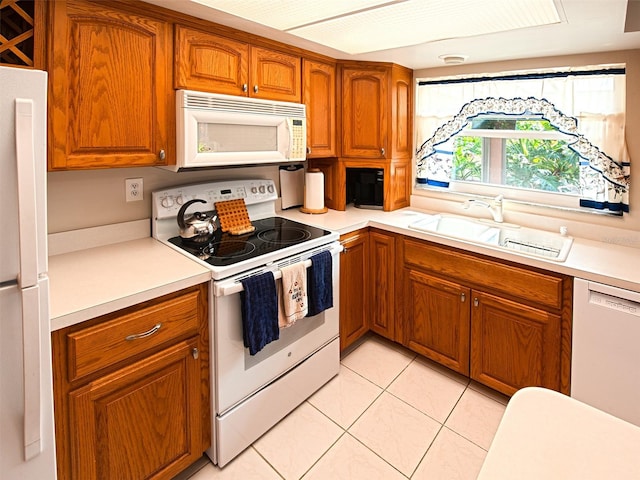 kitchen with light countertops, white appliances, a sink, and brown cabinets