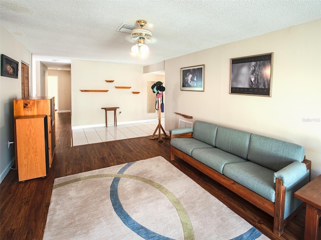 living area featuring a textured ceiling, wood finished floors, visible vents, and baseboards