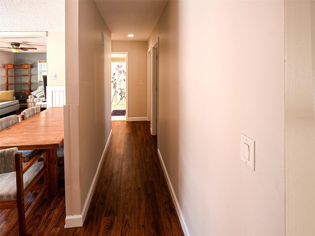 hallway featuring dark wood finished floors, a textured ceiling, and baseboards