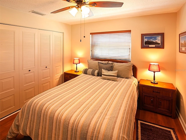 bedroom featuring a textured ceiling, visible vents, a ceiling fan, a closet, and dark wood finished floors