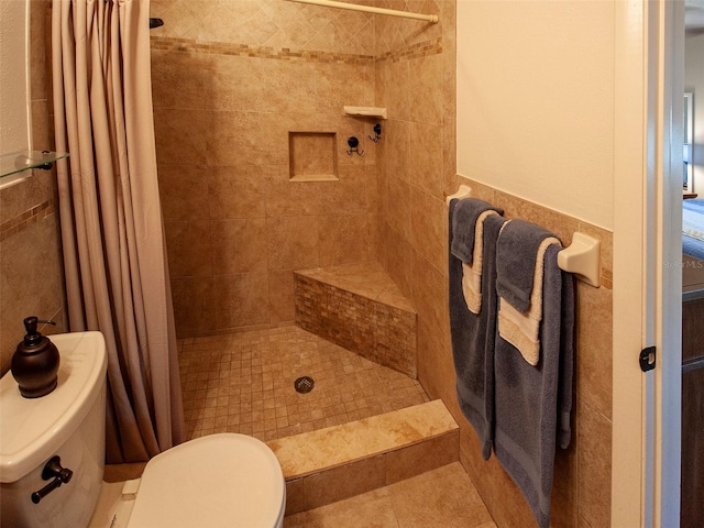 bathroom with wainscoting, a tile shower, tile walls, and toilet