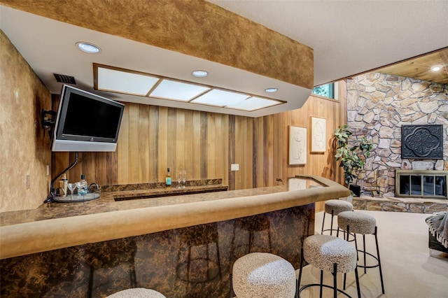 bar featuring recessed lighting, a stone fireplace, wooden walls, and a bar