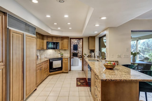 kitchen with a breakfast bar area, a sink, light stone countertops, a peninsula, and black appliances