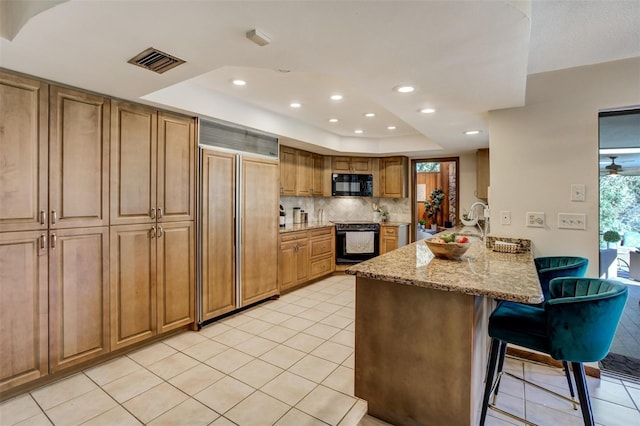 kitchen featuring visible vents, light stone counters, a kitchen breakfast bar, a peninsula, and black appliances