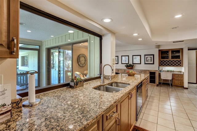 kitchen with brown cabinetry, glass insert cabinets, light stone countertops, a sink, and light tile patterned flooring