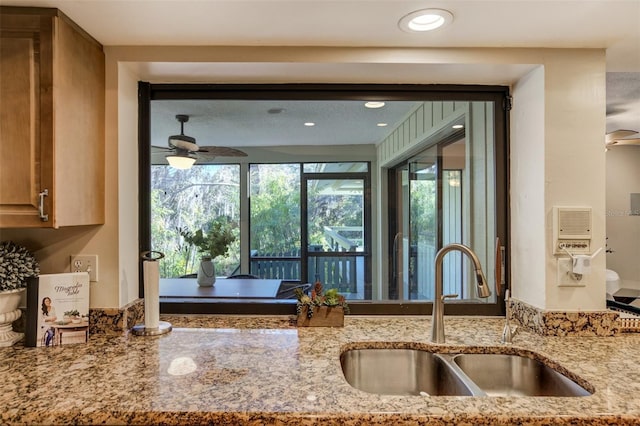 kitchen featuring a ceiling fan, light stone counters, a sink, and recessed lighting