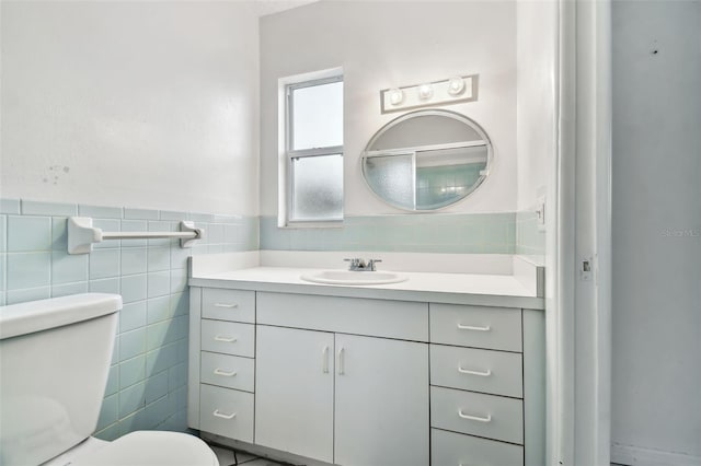 bathroom featuring a wainscoted wall, tile walls, toilet, and vanity