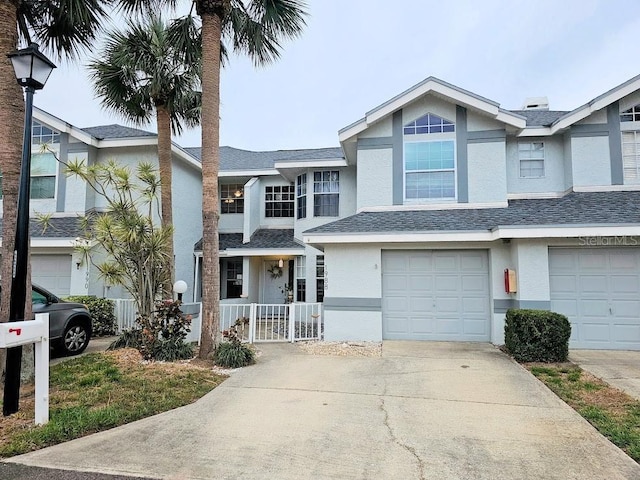 townhome / multi-family property with concrete driveway, roof with shingles, an attached garage, and stucco siding