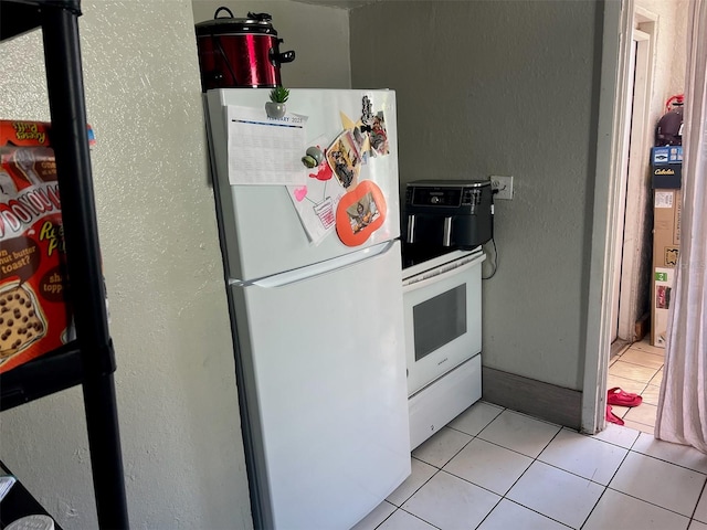 kitchen with a textured wall, light tile patterned floors, and freestanding refrigerator