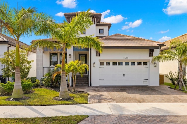 view of front of property featuring a tiled roof, decorative driveway, an attached garage, and stucco siding