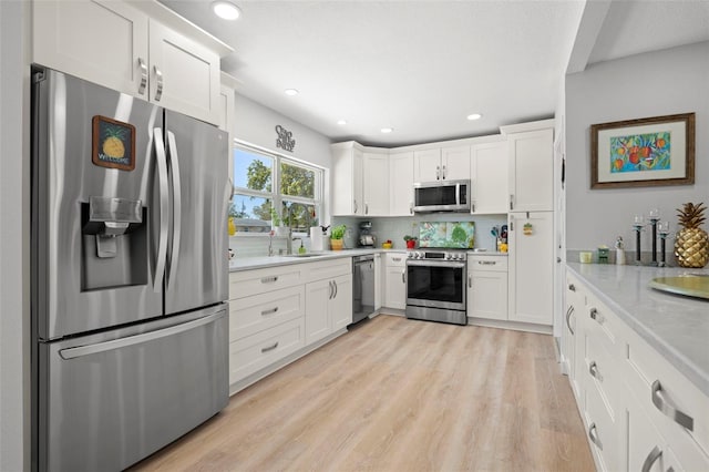 kitchen featuring light wood-style flooring, stainless steel appliances, a sink, white cabinetry, and decorative backsplash