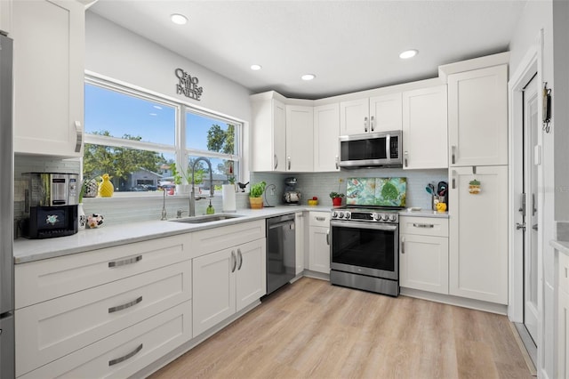 kitchen with appliances with stainless steel finishes, a sink, light wood-style flooring, and white cabinets