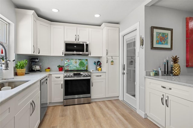 kitchen with stainless steel appliances, light countertops, light wood finished floors, and white cabinetry