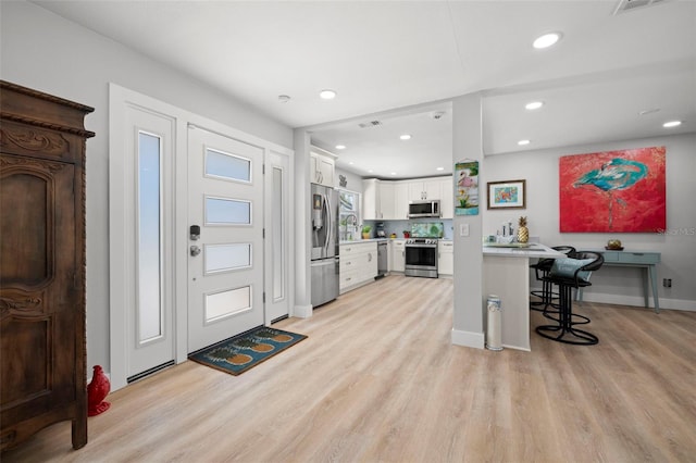 foyer with baseboards, light wood-type flooring, visible vents, and recessed lighting