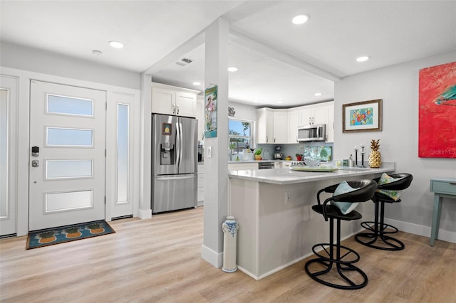 kitchen with a peninsula, white cabinetry, a kitchen breakfast bar, appliances with stainless steel finishes, and light wood-type flooring