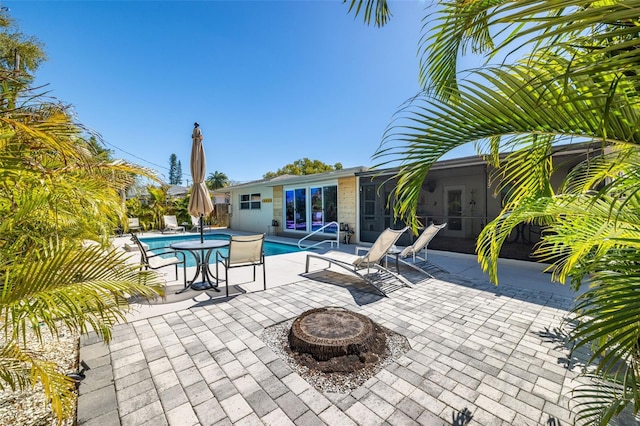 view of patio / terrace featuring an outdoor fire pit, a sunroom, and an outdoor pool