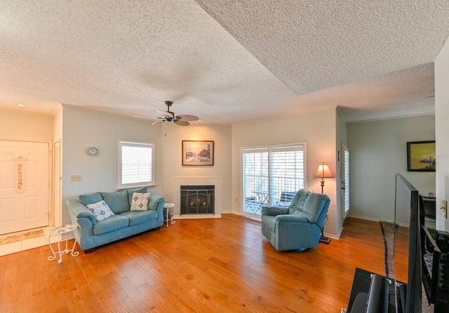 living area featuring a textured ceiling, a tile fireplace, wood finished floors, a ceiling fan, and baseboards