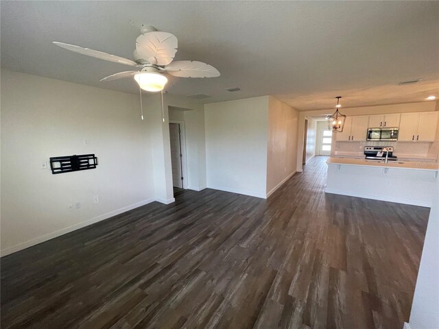 unfurnished living room with ceiling fan with notable chandelier, dark wood finished floors, visible vents, and baseboards