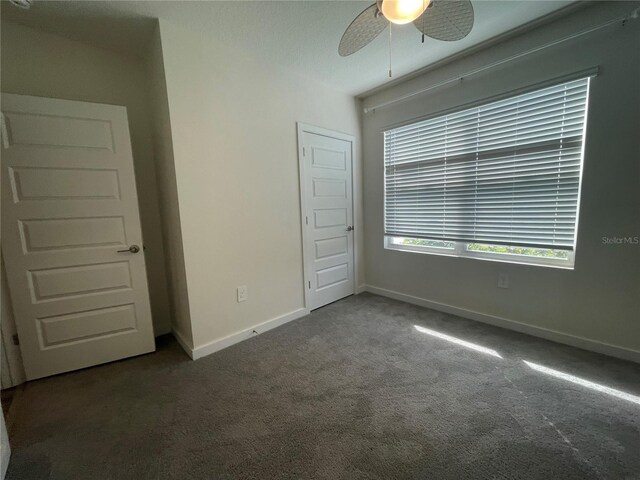 unfurnished bedroom with ceiling fan, baseboards, and dark colored carpet