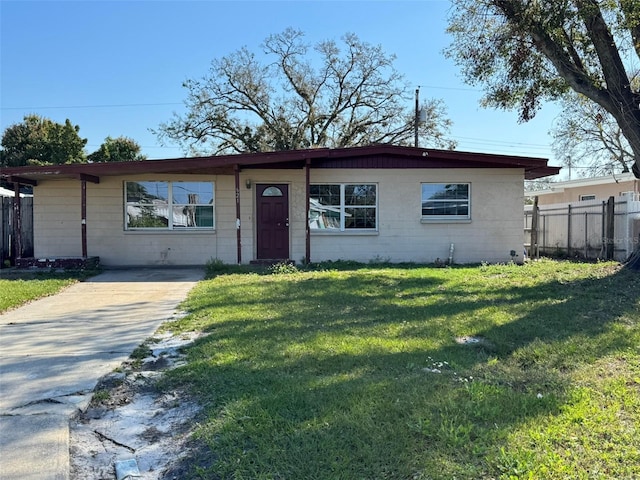 view of front of house with a front yard, concrete block siding, and fence