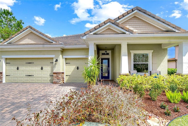 craftsman inspired home featuring a garage, decorative driveway, a tile roof, and stucco siding