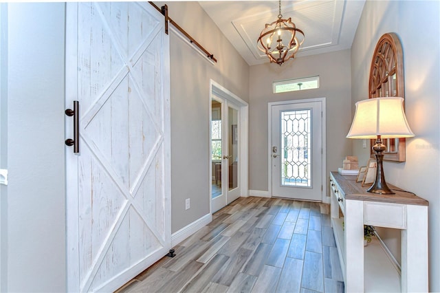 entryway with light wood-style floors, a chandelier, baseboards, and a barn door