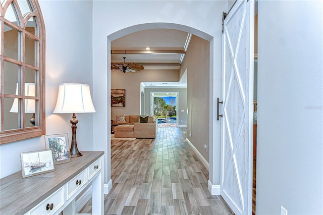 hall with arched walkways, a barn door, light wood-style flooring, and baseboards