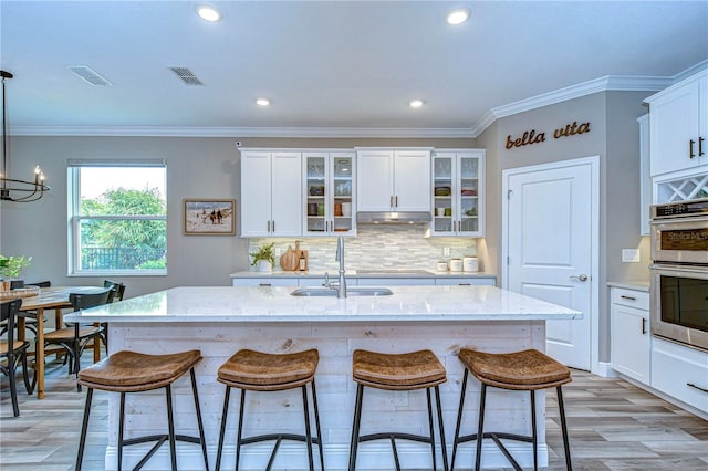 kitchen featuring stainless steel double oven, under cabinet range hood, a sink, visible vents, and a kitchen bar