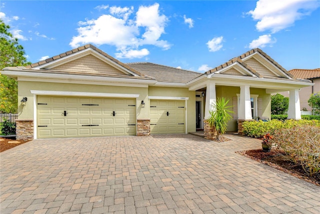 craftsman house with a garage, stone siding, decorative driveway, and stucco siding