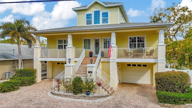 coastal home with decorative driveway, covered porch, central AC, a garage, and stairs